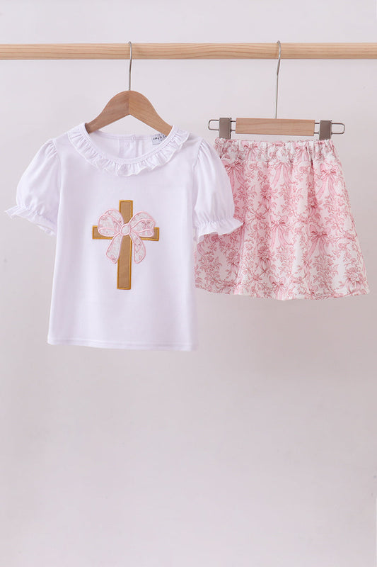 White shirt with floral cross design and pink floral skirt on hangers against a white background