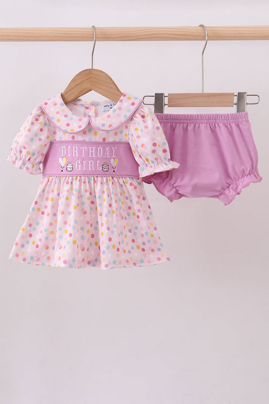 Baby girl's outfit with polka dot dress and pink bloomers on a hanger against a white background